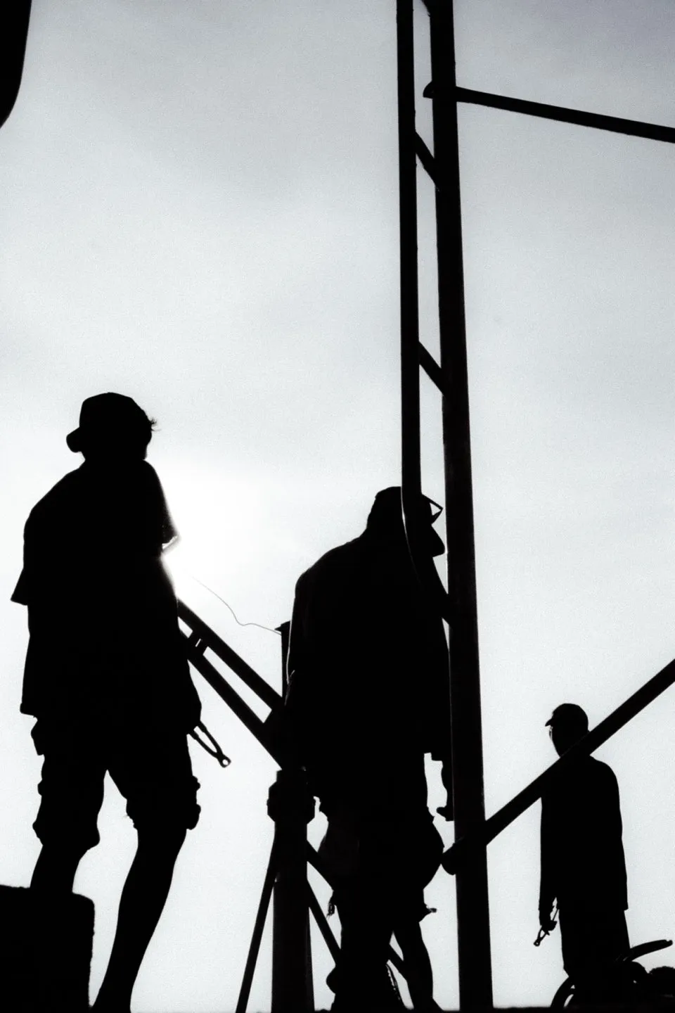 A construction worker silhouetted beside a steel frame against a bright sky.