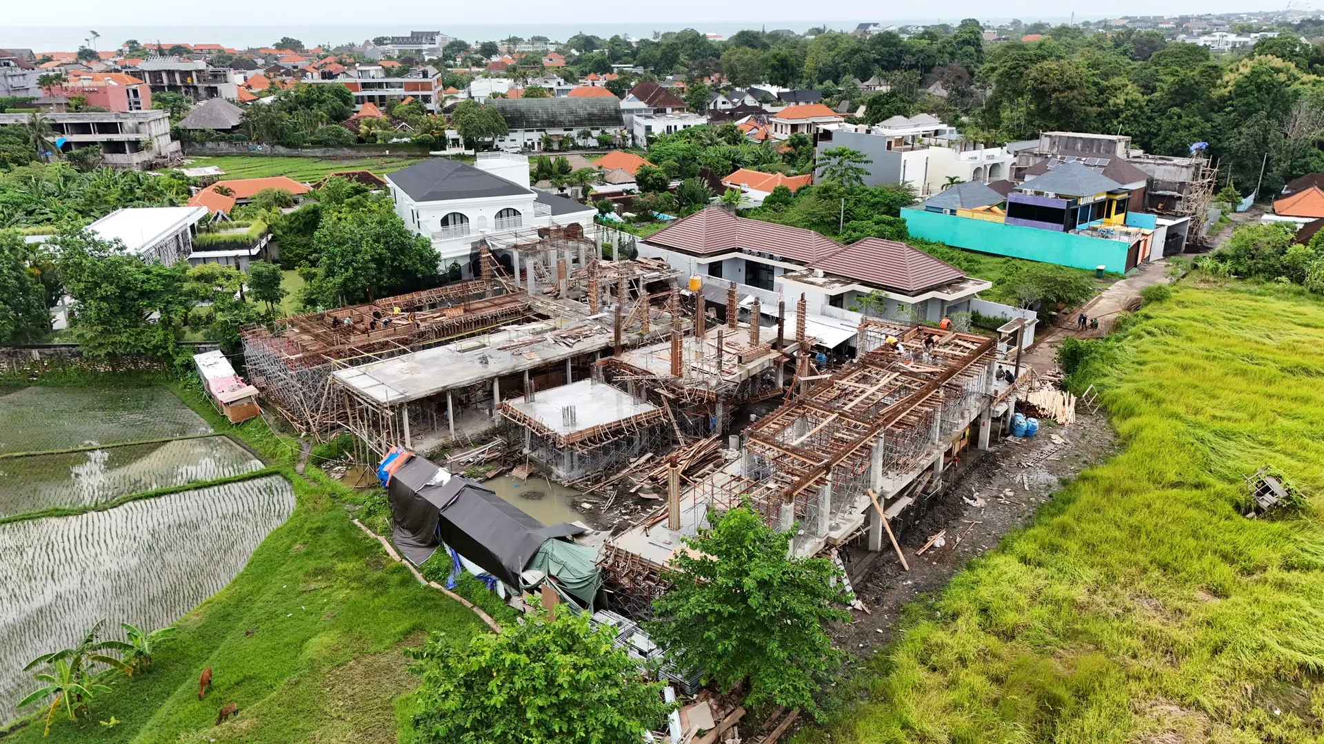 Aerial view of a villa’s concrete structure and scaffolding among rice fields and homes.