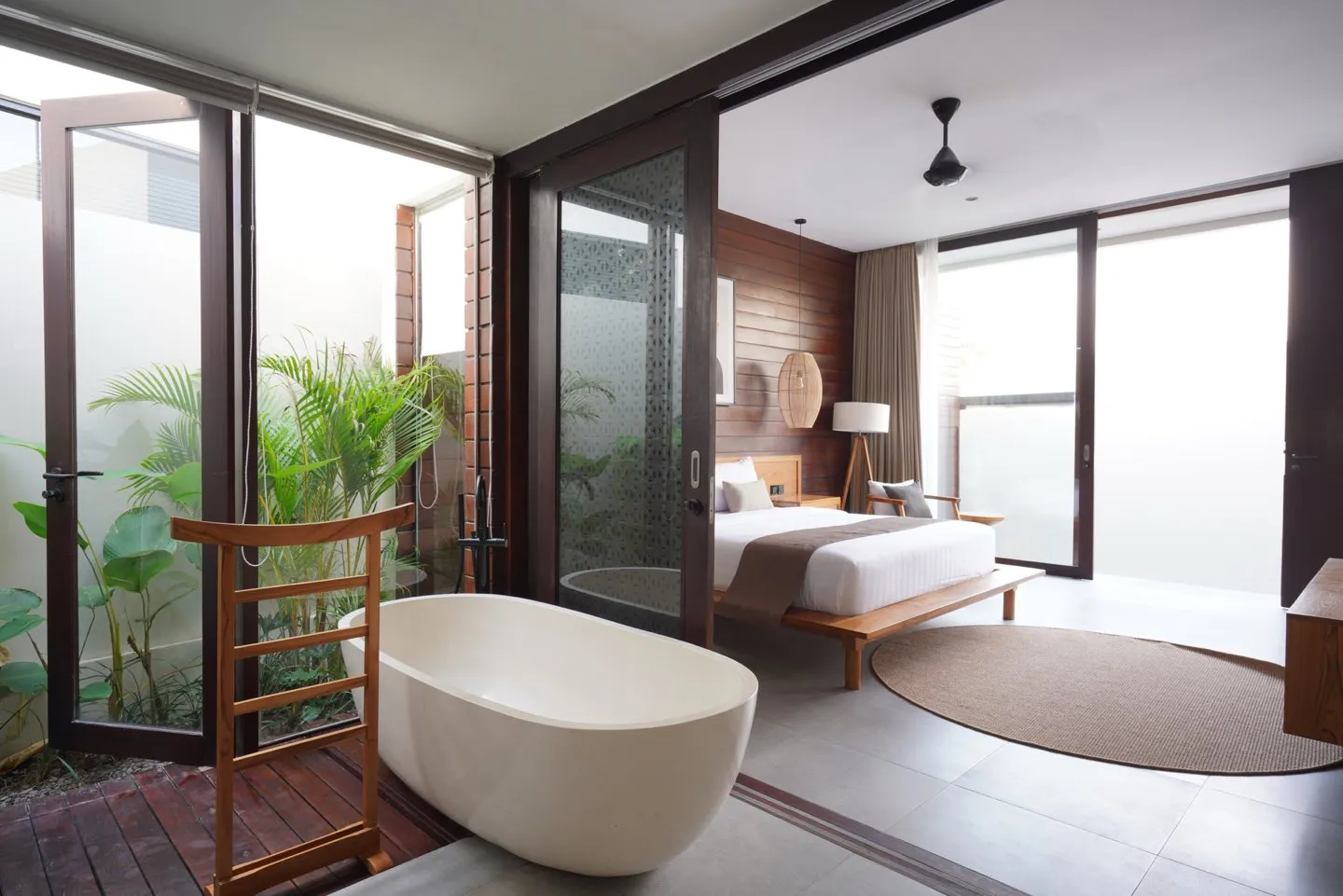 A bedroom with a white bathtub beside glazing and a small garden.