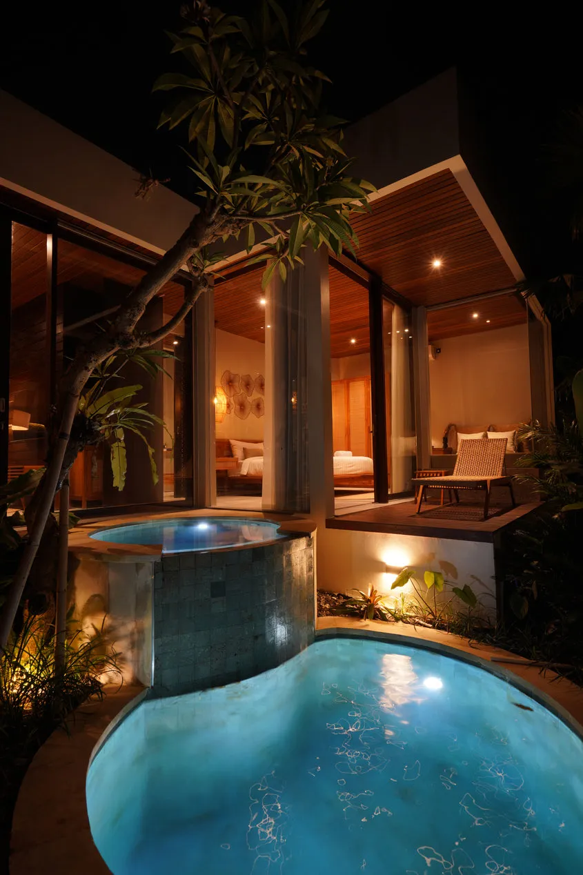 A small illuminated pool at night beside a pavilion with a timber ceiling.