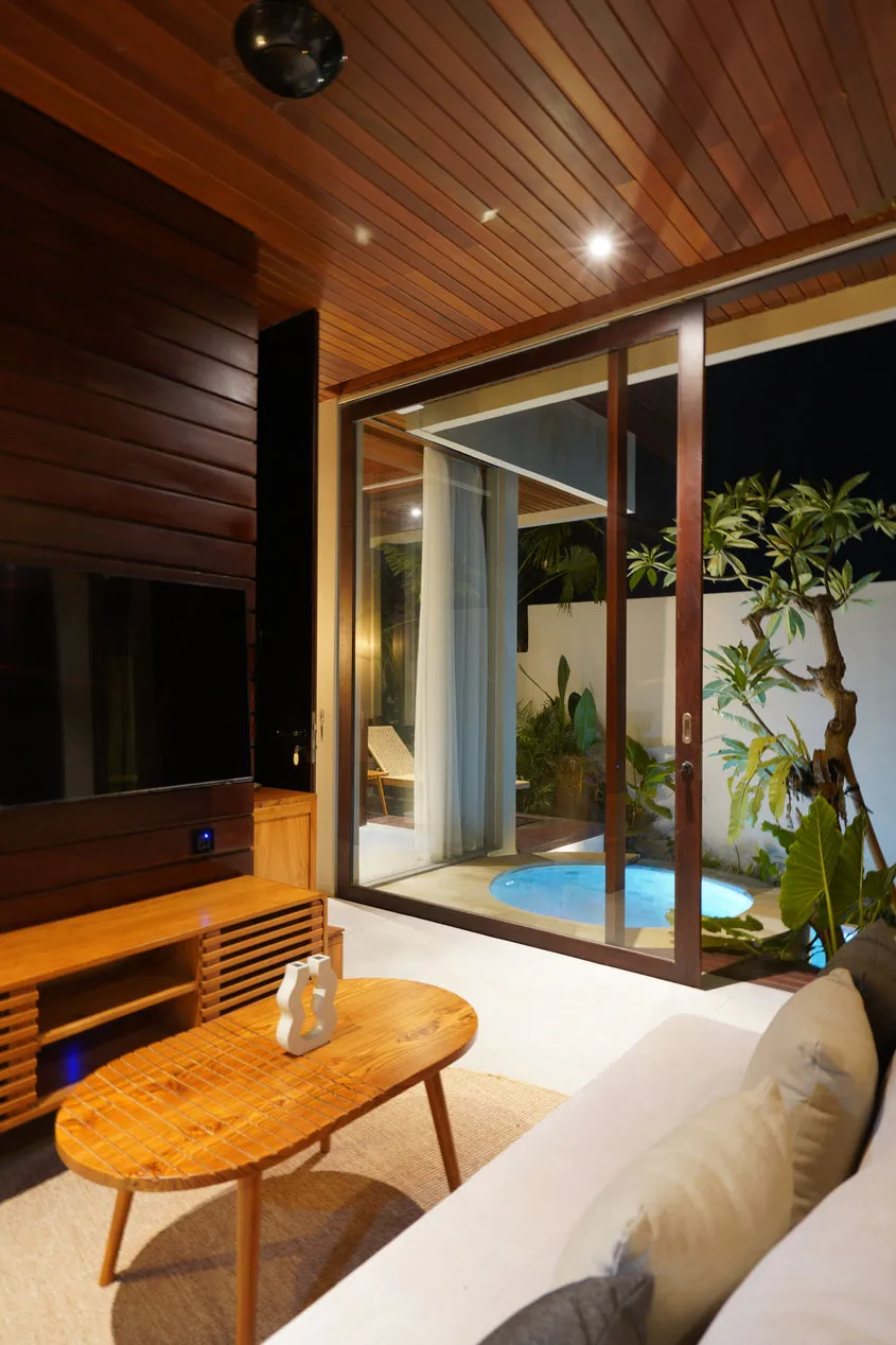 A timber-panelled living room with large windows facing a small pool.