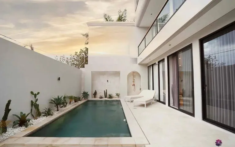 A long swimming pool in the courtyard of a white building at dusk.