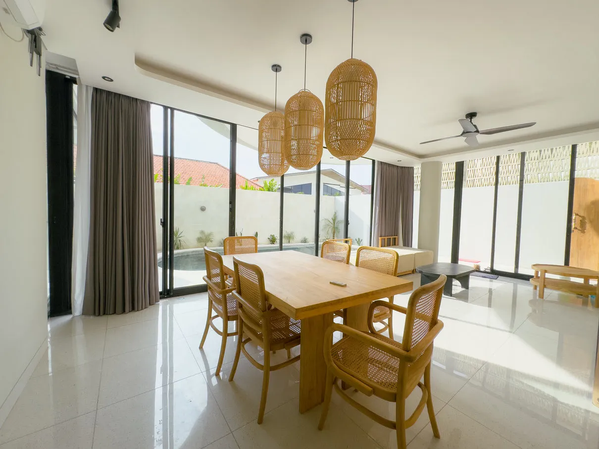 A dining room with a timber table, woven lamps and large glazed windows.