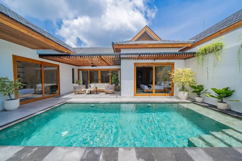 A swimming pool beside a timber-roofed villa in daylight.