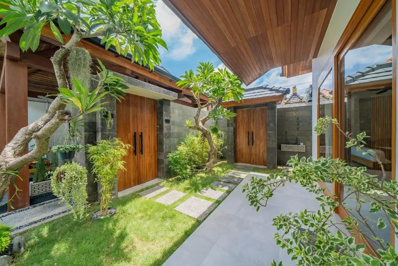 A garden with a frangipani tree and timber doors leading to a bedroom.