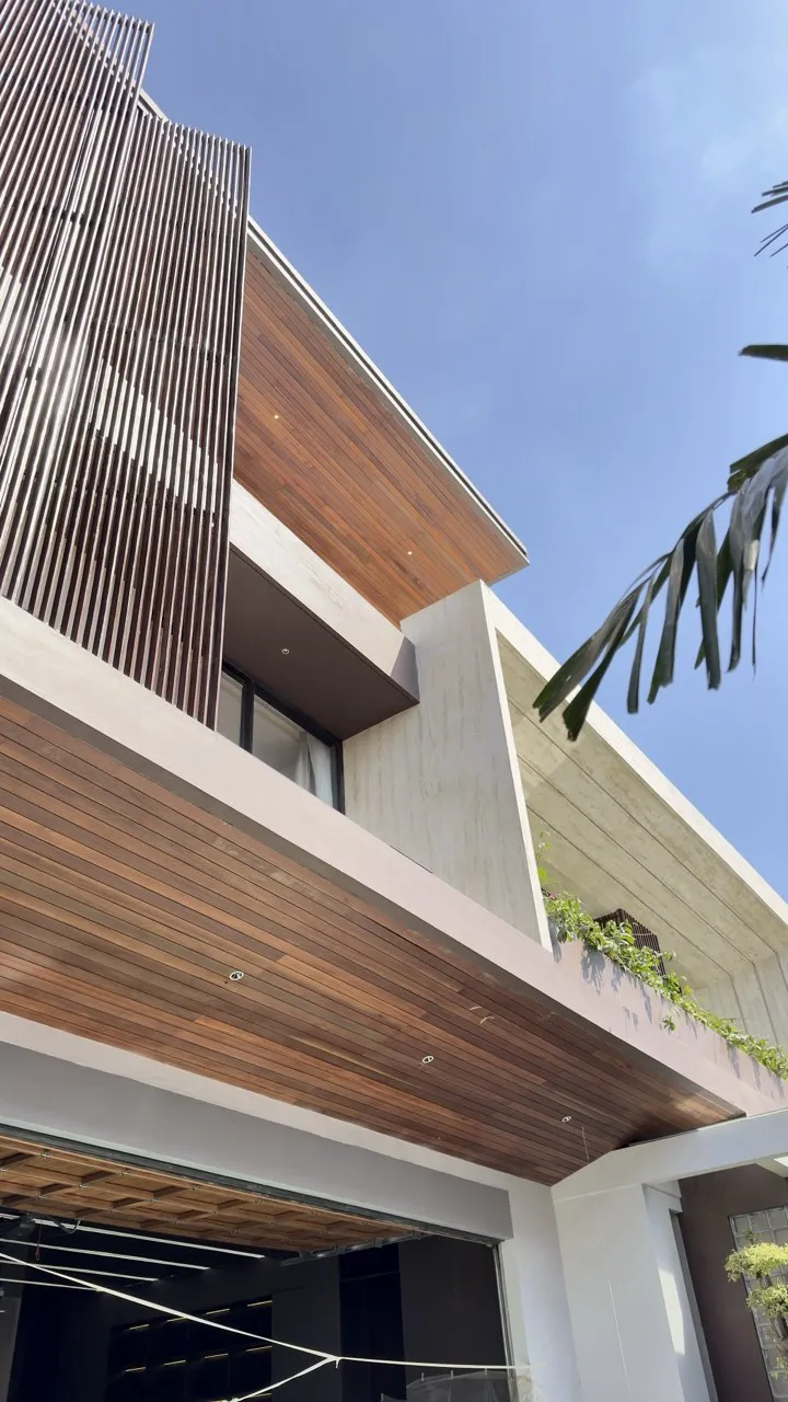 An exposed concrete facade with timber screens and a projecting timber ceiling beneath a blue sky.