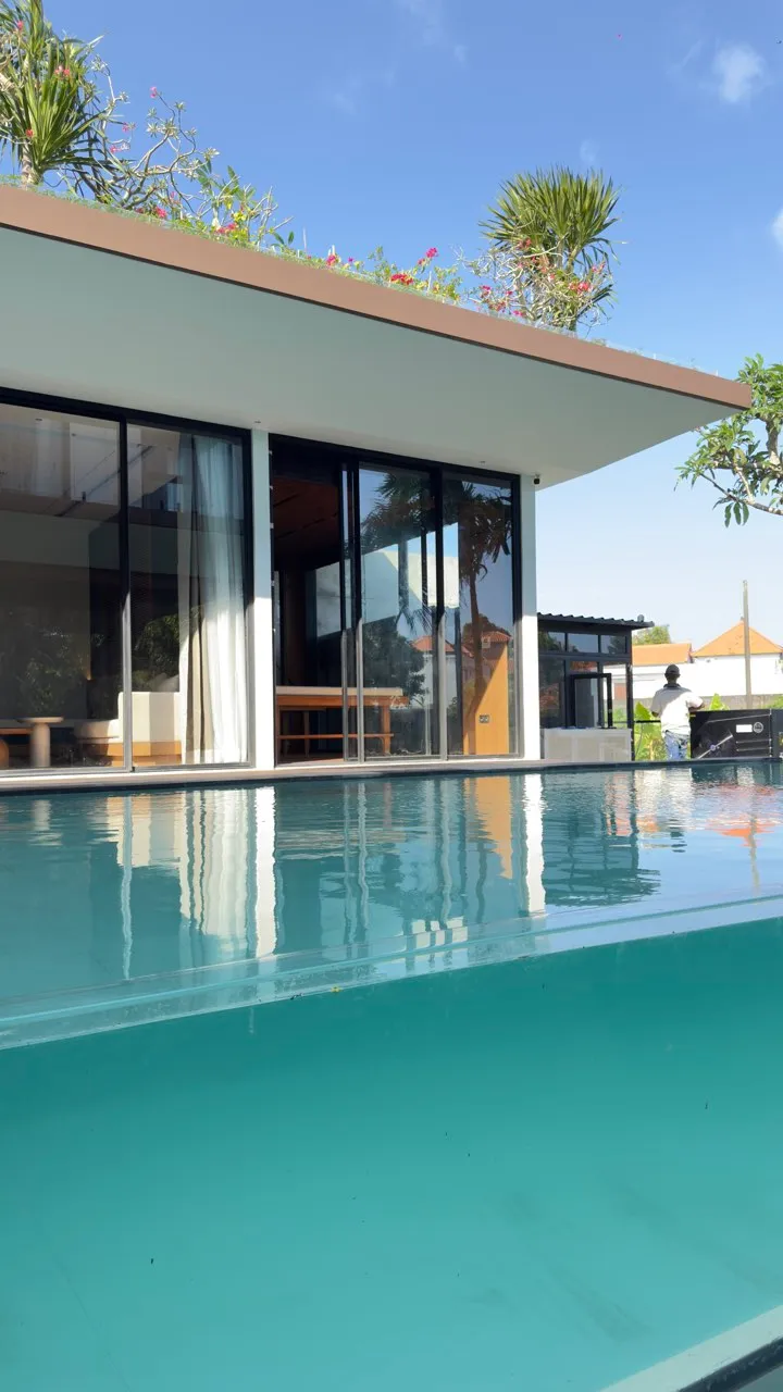 A swimming pool beside the villa’s glazed openings and concrete roof canopy.