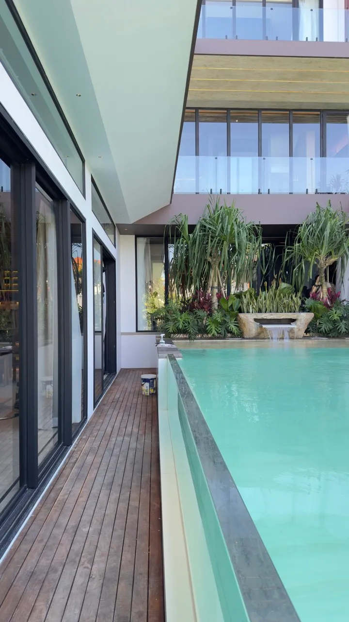 A timber pool deck with tropical plants and glazed openings over two levels.