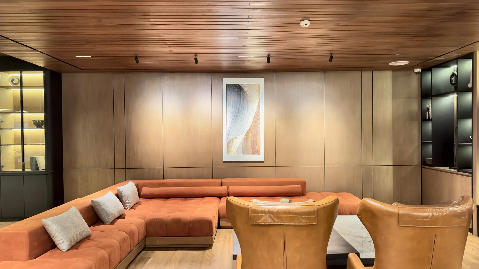 A lounge with timber ceilings and wall panels, an orange sofa and leather chairs.