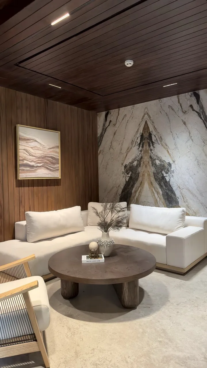 A lounge with patterned marble walls and white sofas beneath a timber ceiling.