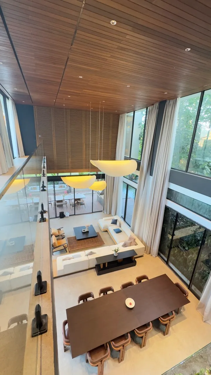 An overhead view of a double-height living and dining space with timber ceilings and pendant lights.