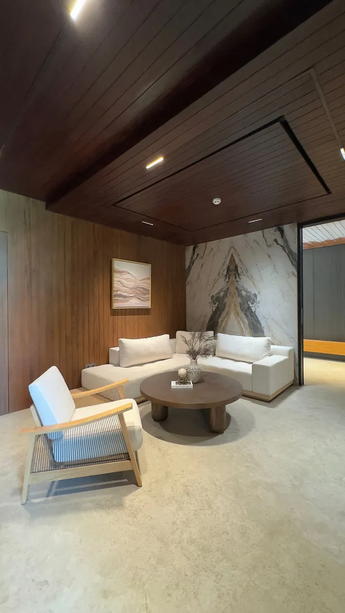 A sitting area with a timber ceiling, sofa and white chairs.