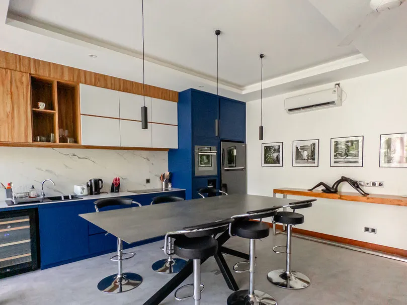 A kitchen with blue and timber cabinetry and a long counter with bar stools.