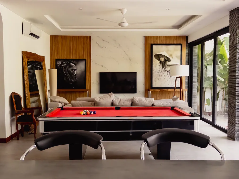 A lounge with a red pool table and a sofa behind it.
